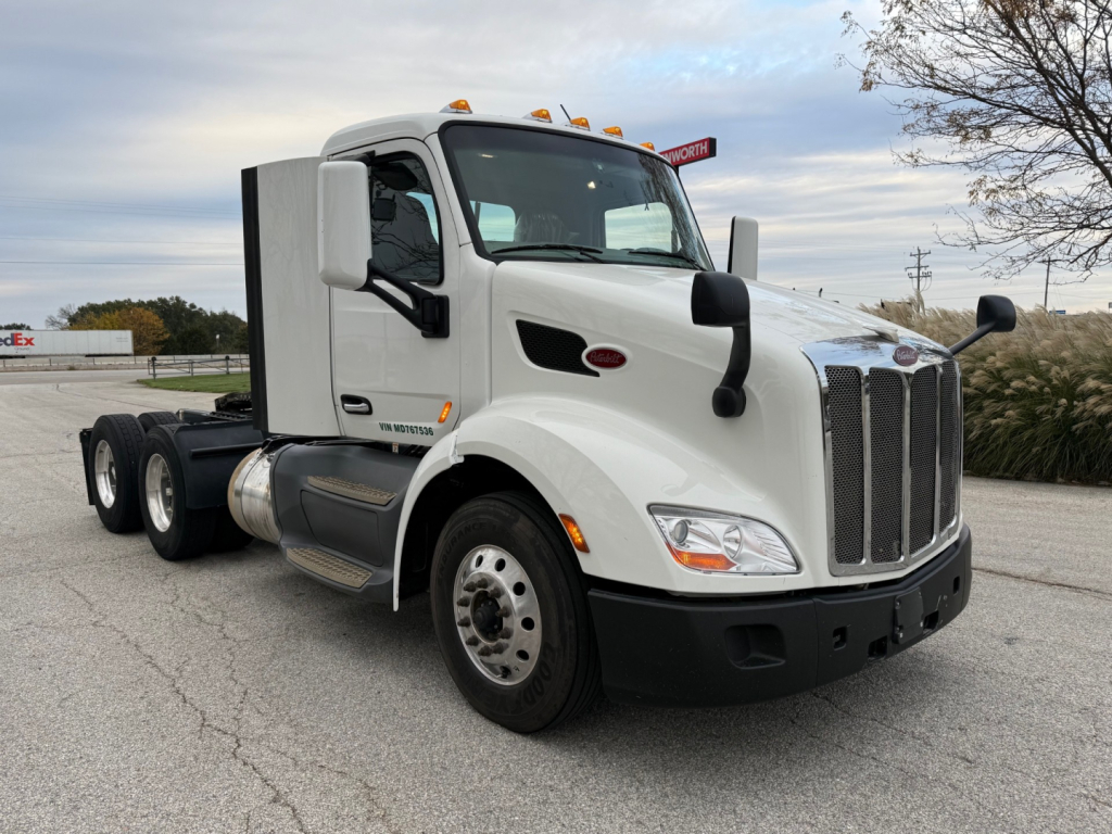 Peterbilt 579 daycab truck front-left view showing chrome grille, white cab, side mirrors, and dual rear axles. Visible text includes Peterbilt badge on hood and model 579 on door.