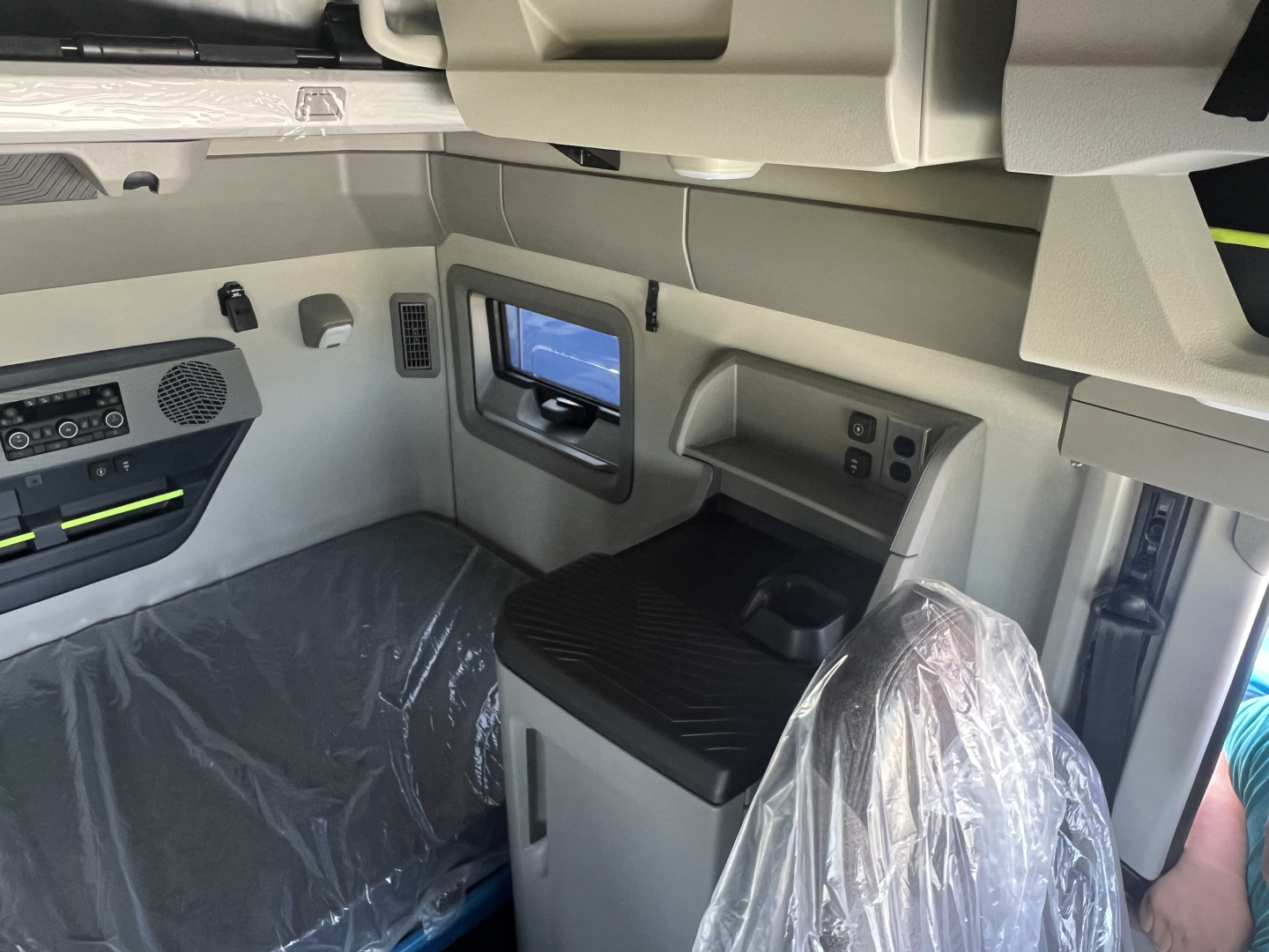 Volvo VNL64T860 truck cab interior showing control panel, storage, and a mounted screen viewer. Plastic-covered seats and clean gray trim.