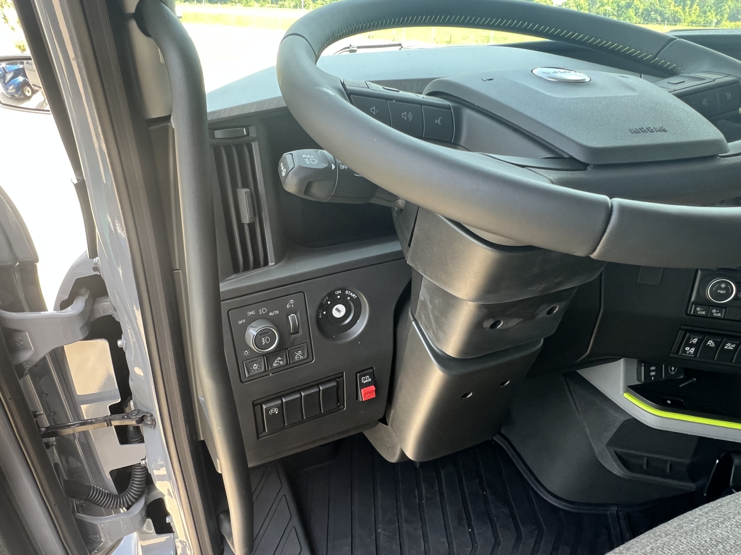 Volvo truck interior dashboard and steering wheel with control knobs and switches visible on left side; partial visibility of steering column and dashboard panels.