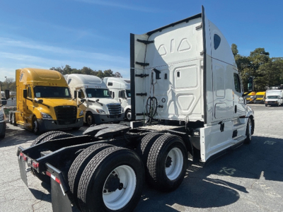 Tractor truck cab in white with dual rear axles and detached fifth wheel, Freightliner Cascadia style, side view showing rear wheels and sleeper cab.