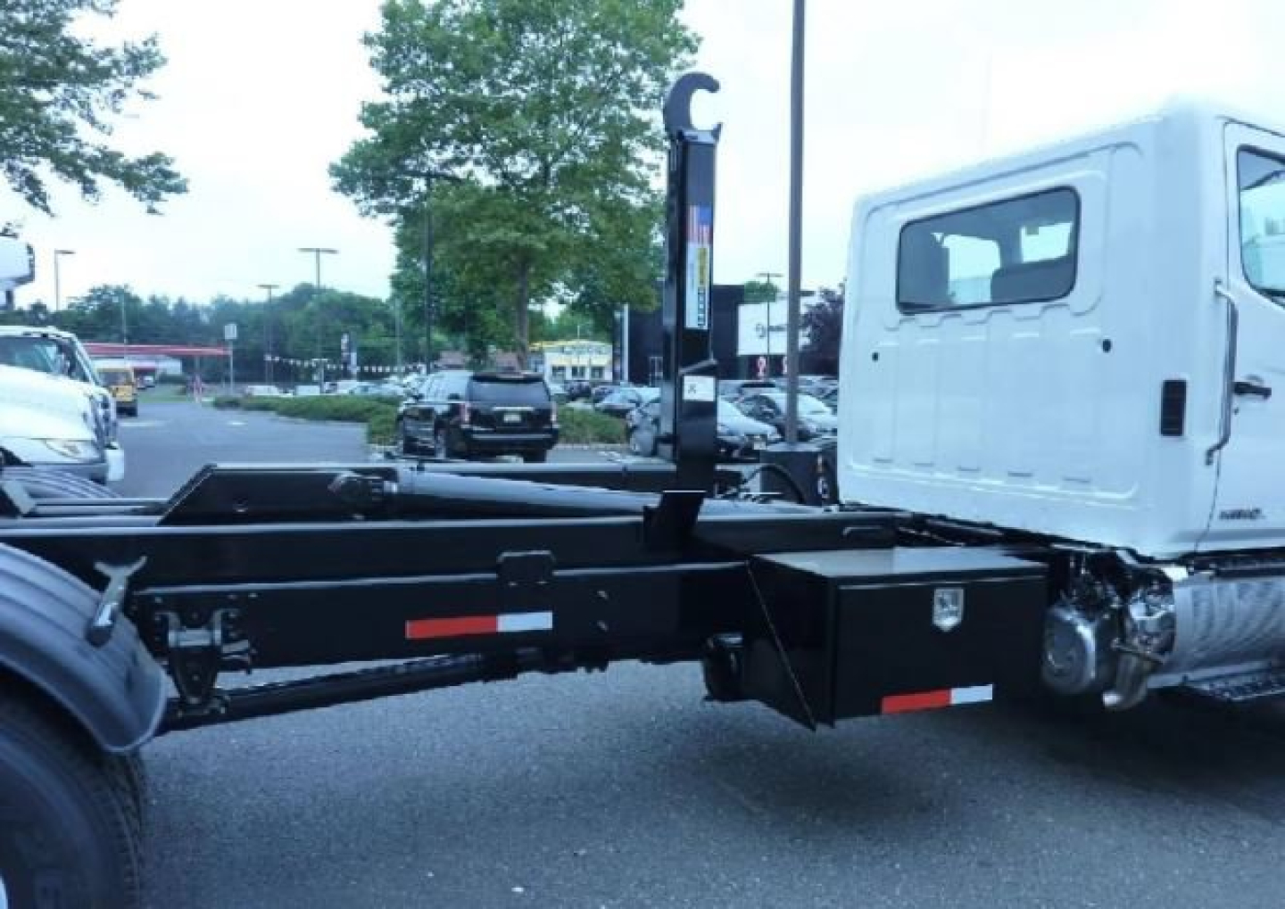 Truck chassis with hooklift system and cab visible, side view showing mounting frame and hydraulic components.