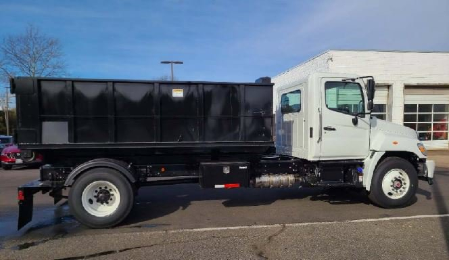 Truck side view showing a white cab and black dump bed with a hooklift system.