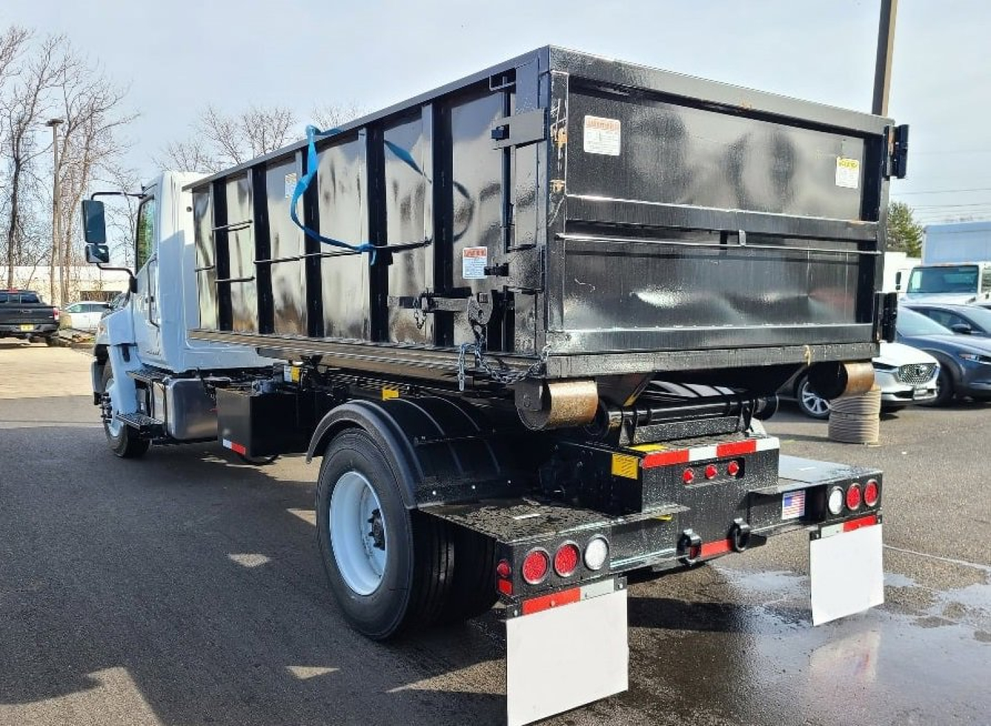 Hino L7 hooklift truck rear view showing dump bed and dual rear wheels with mud flaps and tail lights.