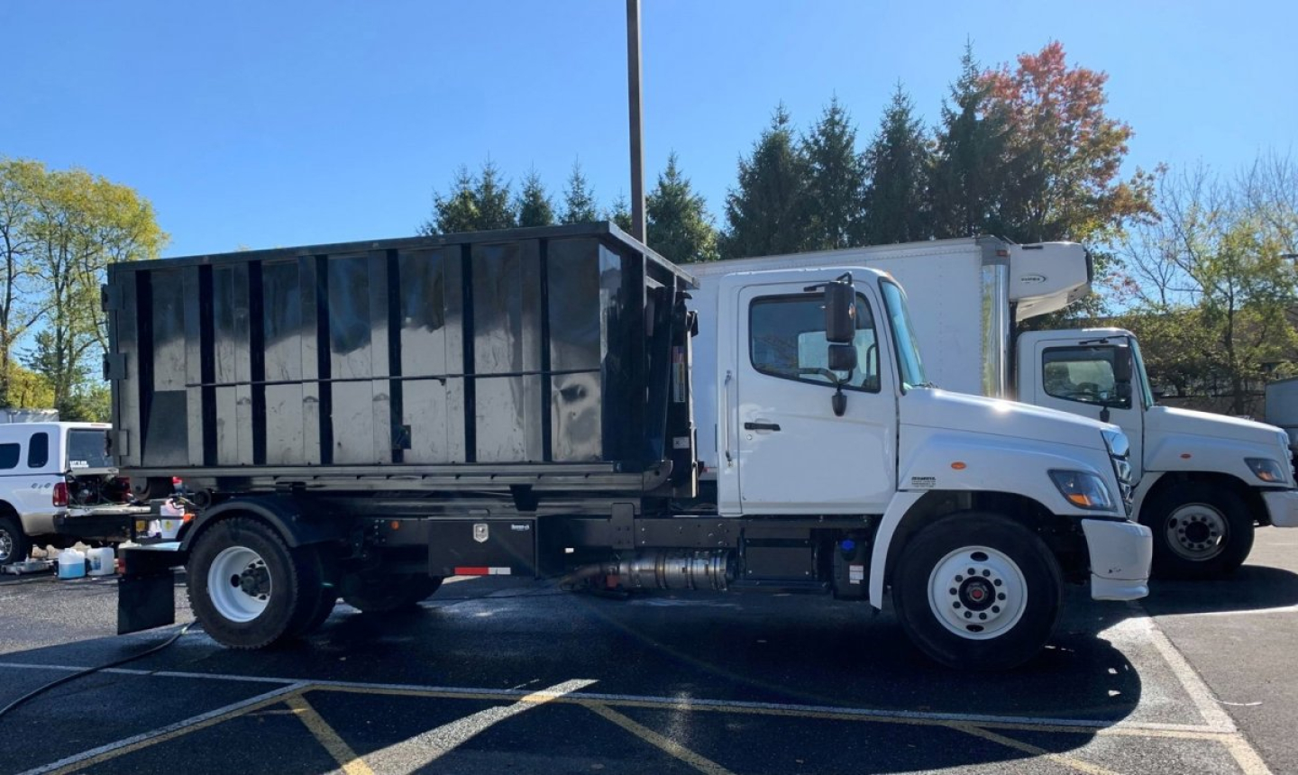 Truck side view showing a white cab and black dump body with hooklift configuration on a paved lot.