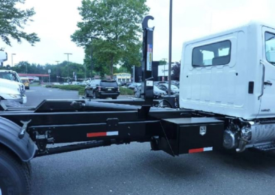 Truck chassis with hooklift system and cab visible, side view showing mounting frame and hydraulic components.