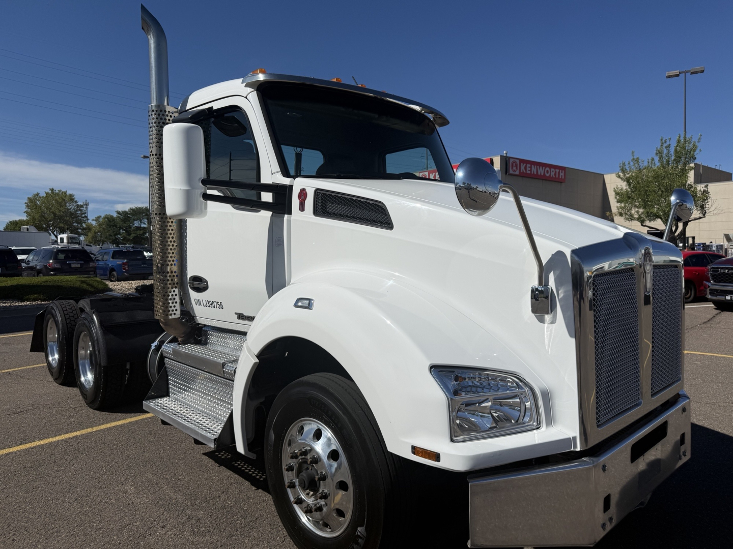 Truck cab showing white 2020 Kenworth T880 with large grille, chrome bumper, dual exhaust stacks, and side steps.