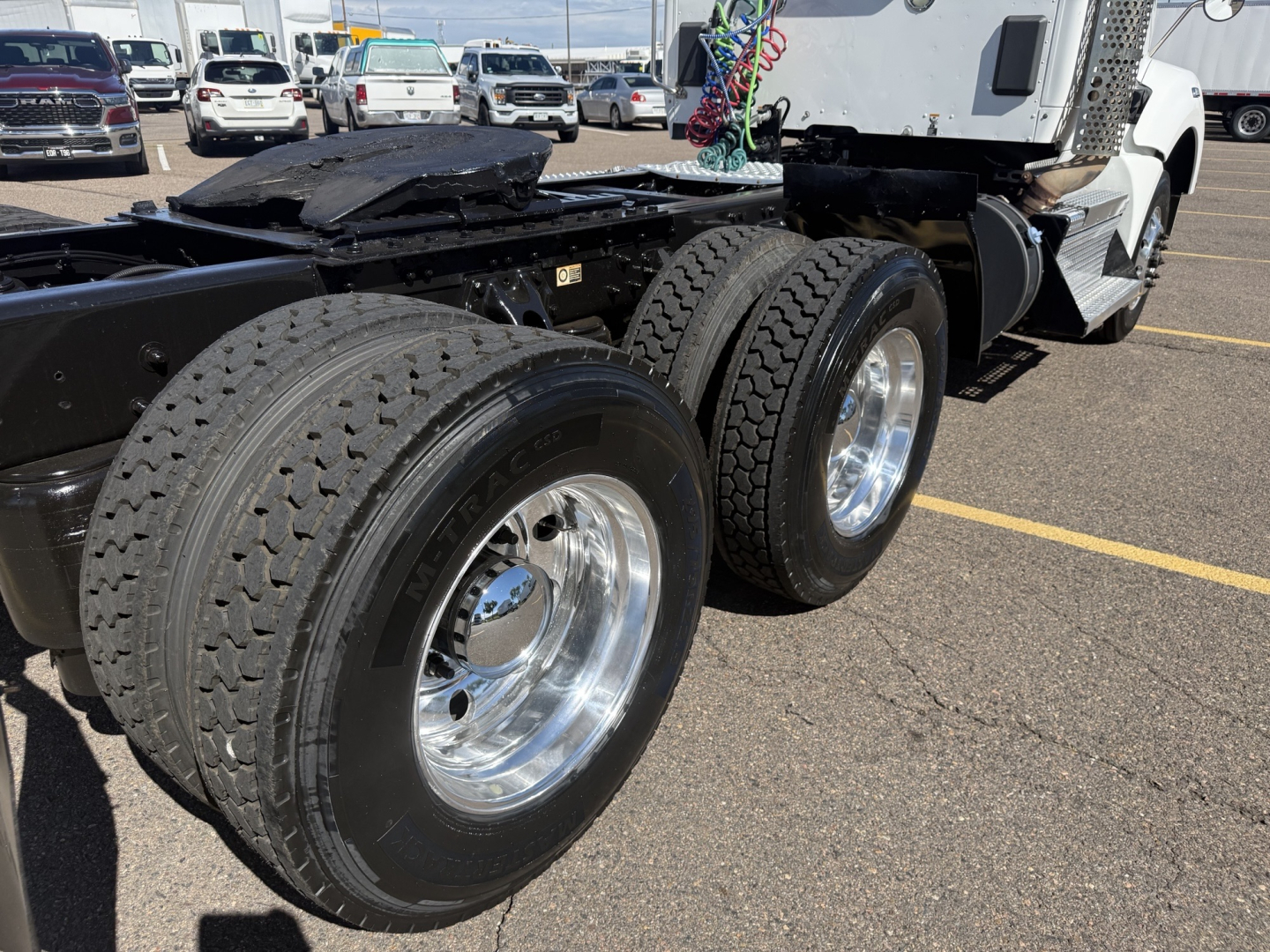 Kenworth T880 wheel end showing dual rear tires with chrome rims; part of the truck chassis and cab behind; no textual labels visible on this view.