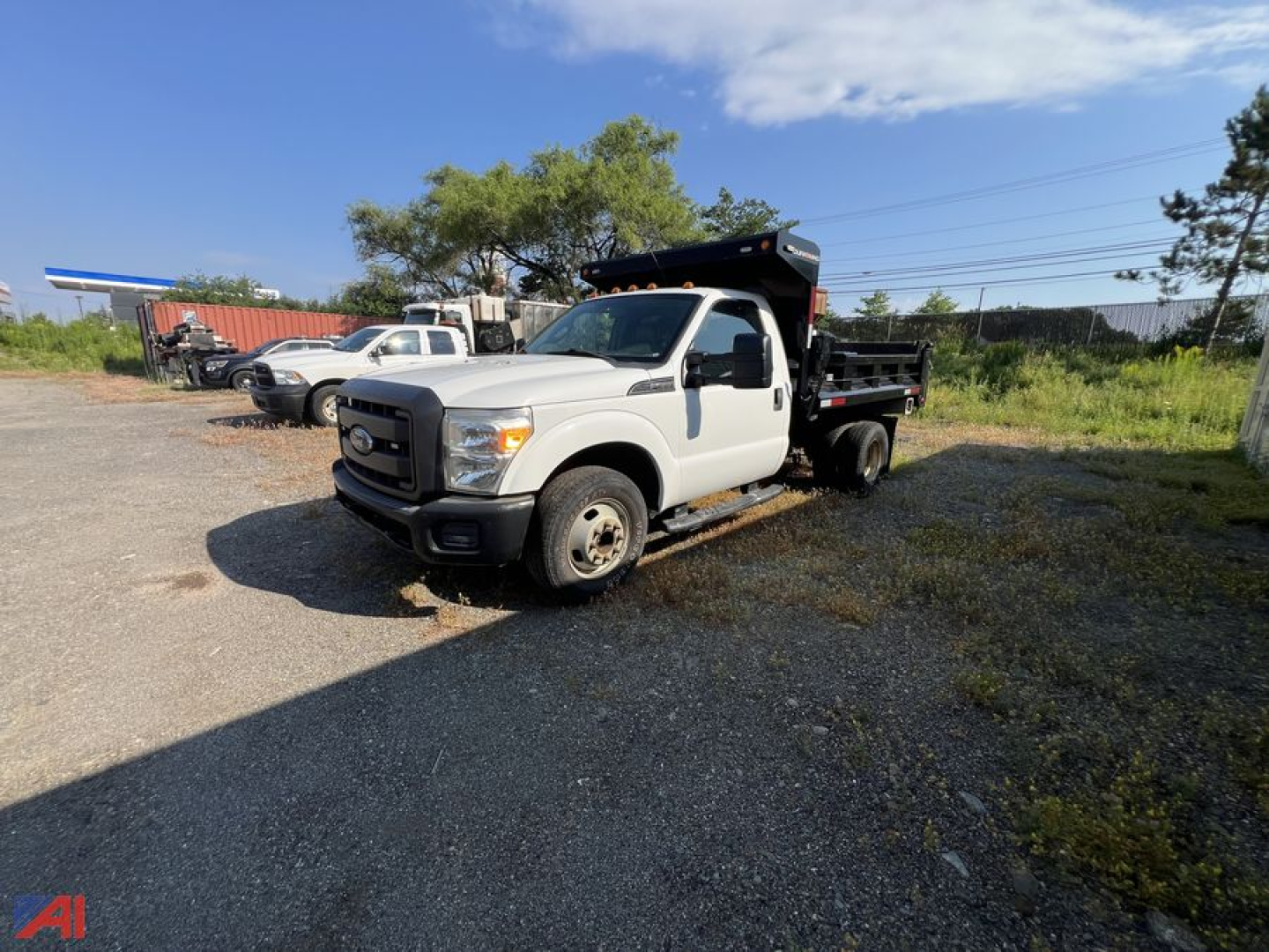 Ford F-350 Super Duty dump truck in a gravel lot, white cab, black dump bed, side view showing front grill