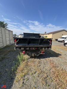 Rear view of a black Ford F-350 Super Duty dump bed. Visible are taillights, hitch, and trailer connections with a gravel lot surface.