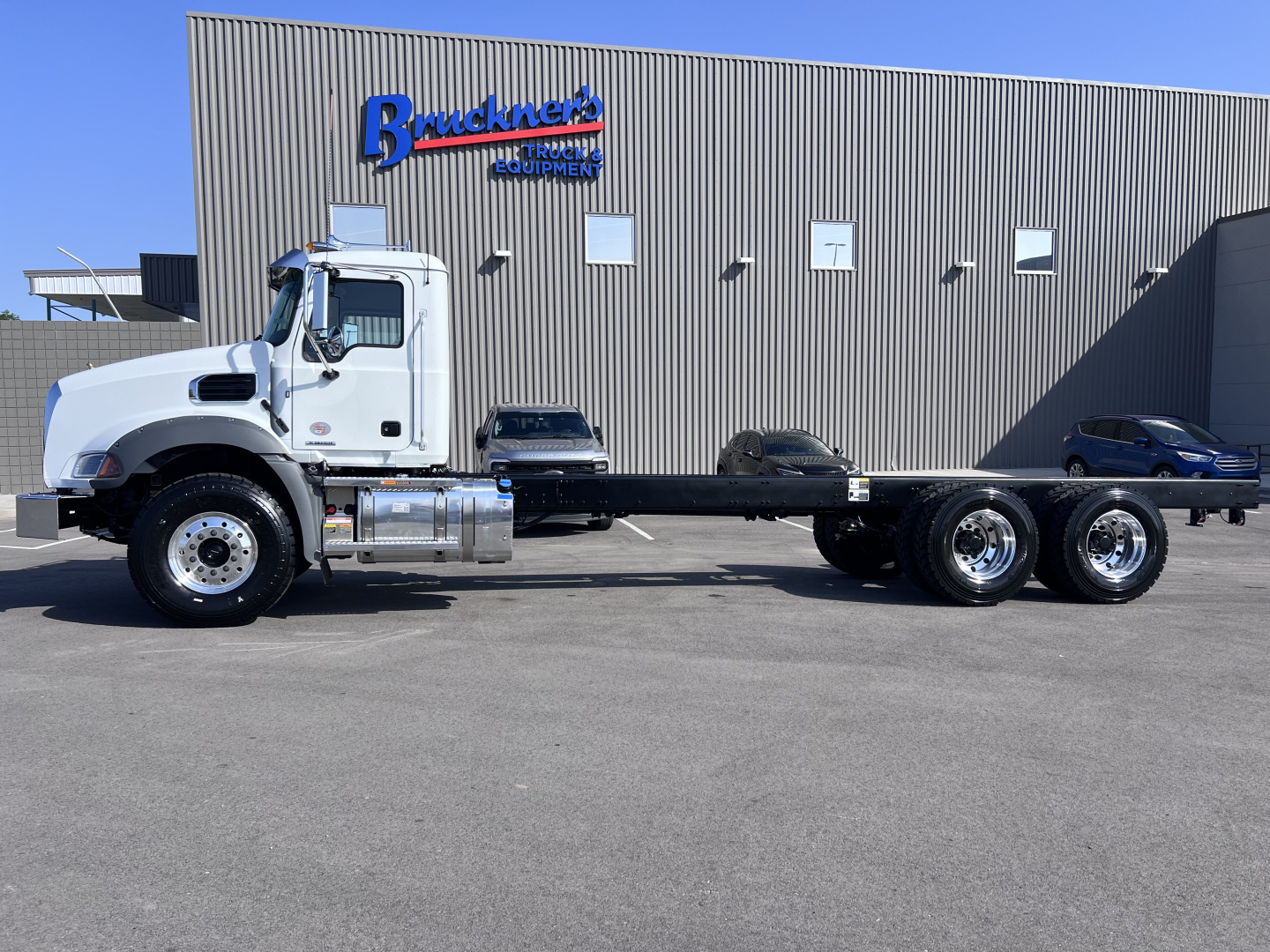 White Mack GR64B tractor cab chassis showing chassis frame and rear wheels with dealership building in background.