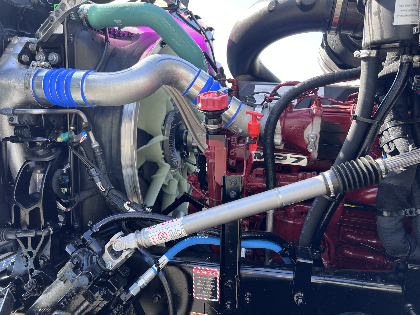 Mack GR64B engine bay showing radiator hoses, coolant reservoir cap, turbo hoses, and engine components with red engine block.