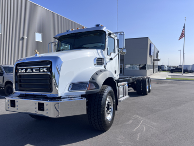 Mack GR64B cab and chassis truck in a light color, front grille shows 'MACK' emblem; chrome bumper; dual rear axles visible behind cab; side mirror, steps, and fender flares visible.