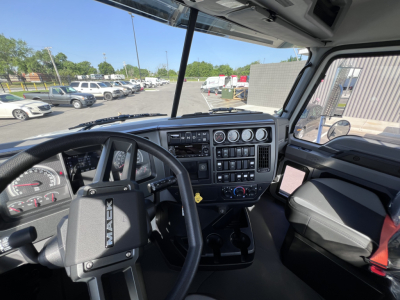 Mack GR64B cab interior showing steering wheel, instrument cluster, dashboard controls, and gear shifter in front of the driver seat.