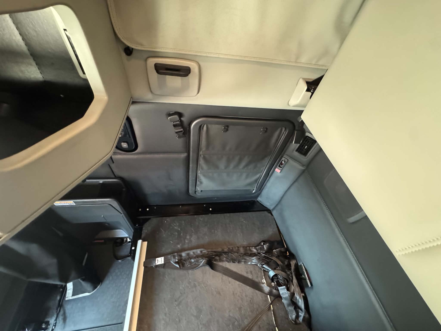 Kenworth T680 cab interior showing sleeper area with collapsed seat belt and side panel storage. View includes door pocket and overhead panel.
