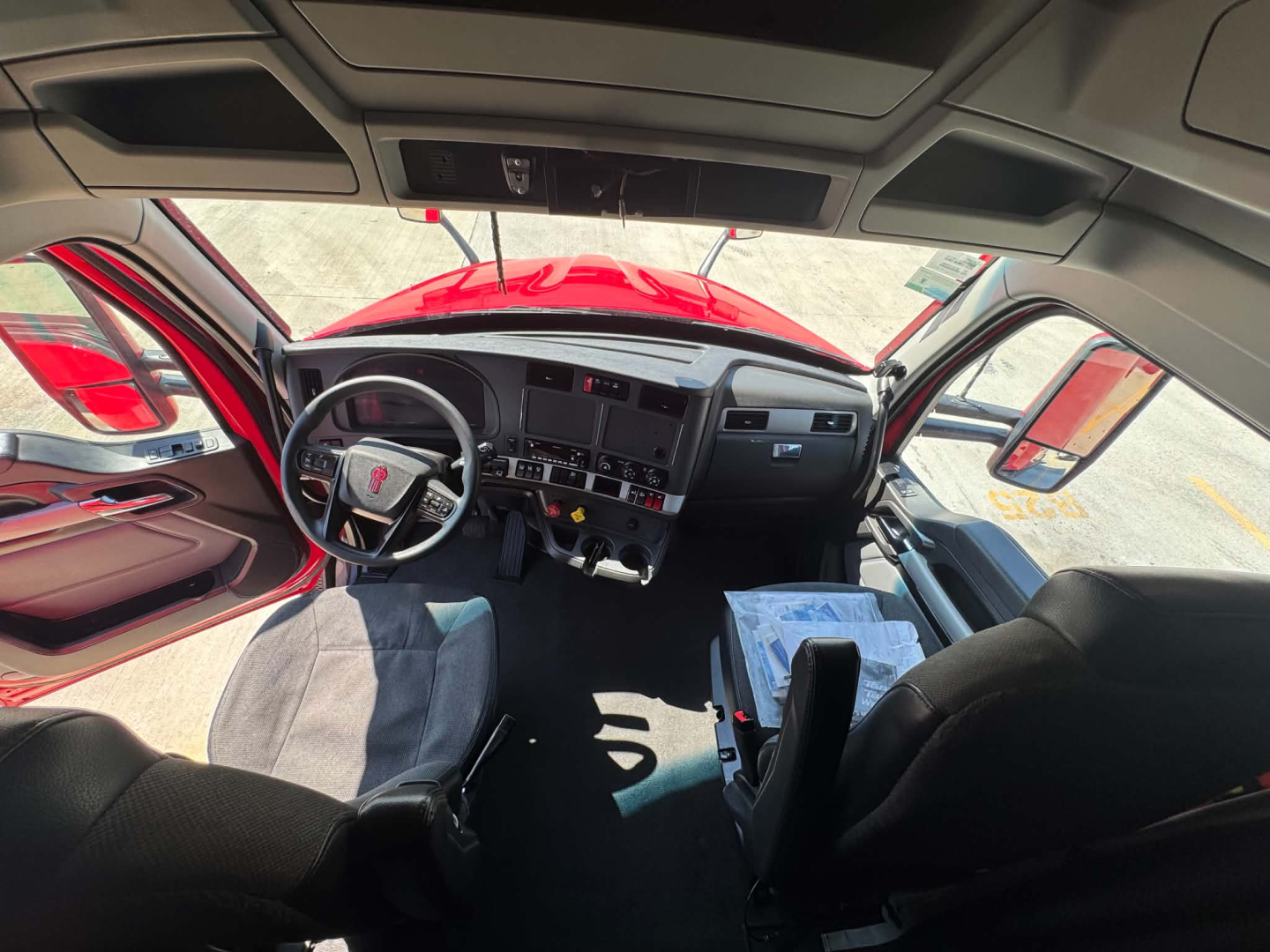Kenworth T680 cab interior view from driver seat showing dashboard, steering wheel, and center console with controls.
