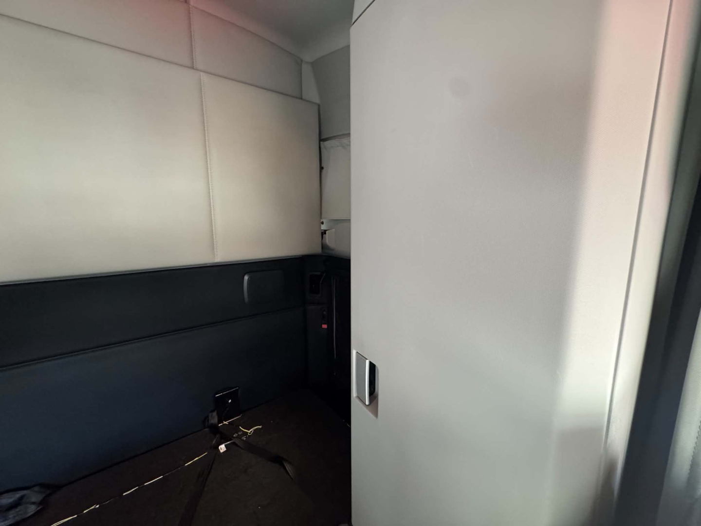 Kenworth T680 sleeper cab interior view showing light gray upholstery and a small storage compartment near a partition.
