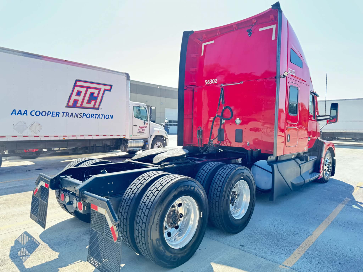 Kenworth T680 sleeper cab tractor showing rear chassis with dual rear axles and red cab; no text visible on side of cab; parking lot background