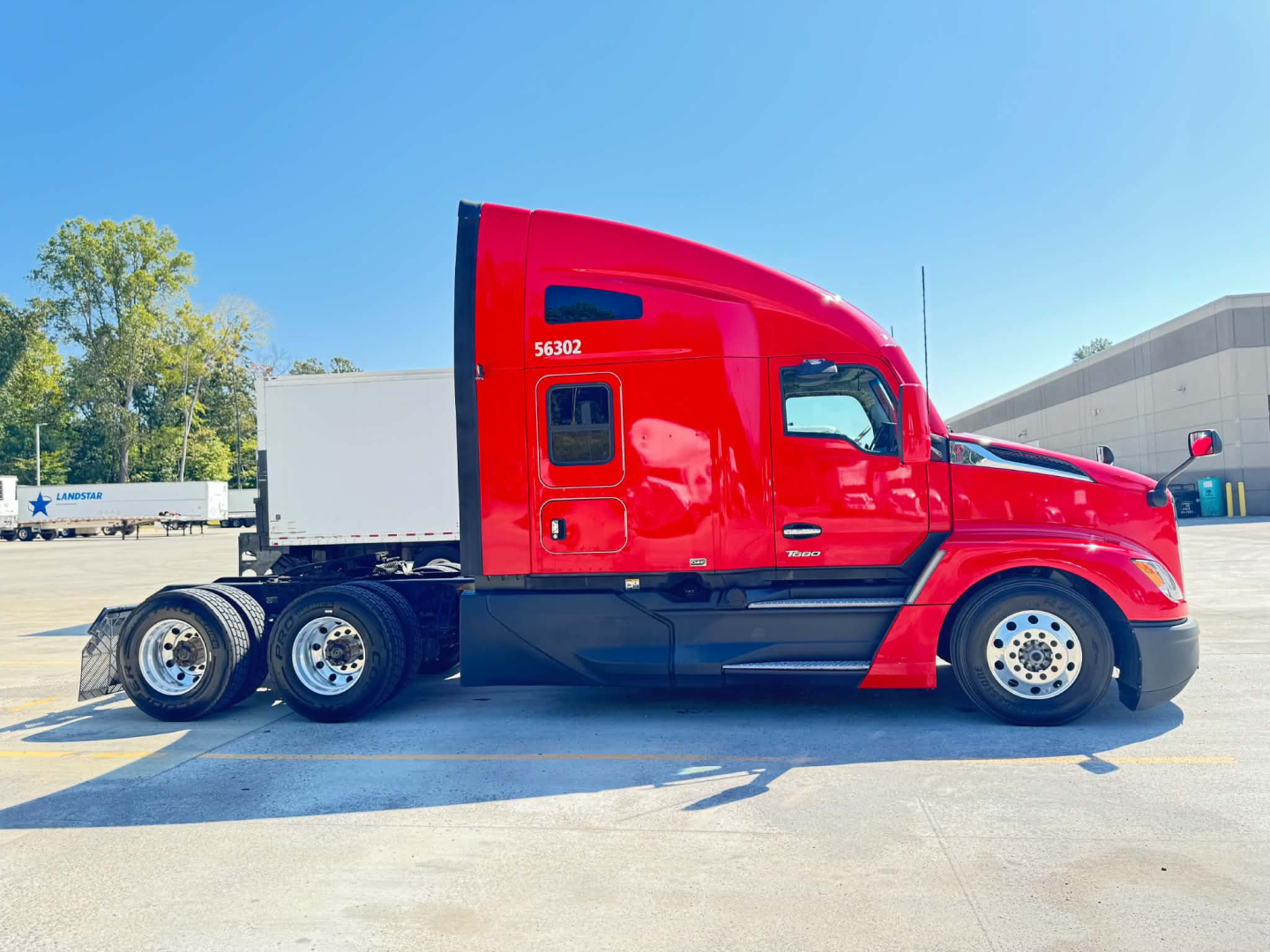 Kenworth T680 truck side view showing red cab and black chassis with triple rear axles.