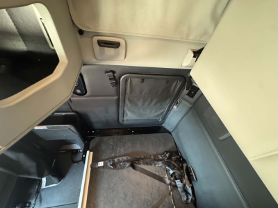 Kenworth T680 cab interior showing sleeper area with collapsed seat belt and side panel storage. View includes door pocket and overhead panel.