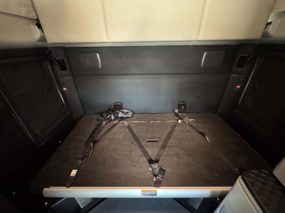 Kenworth T680 interior cargo area with folded rear seats and lashing straps in a sleeper cab showing cargo area and bed platform.