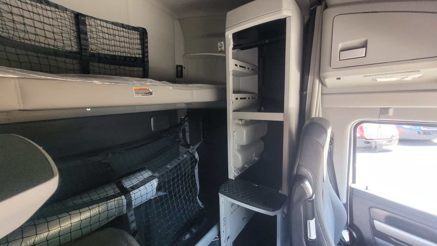 Kenworth T680 cab interior showing sleeper bunk area with overhead storage and open closet/storage compartments.