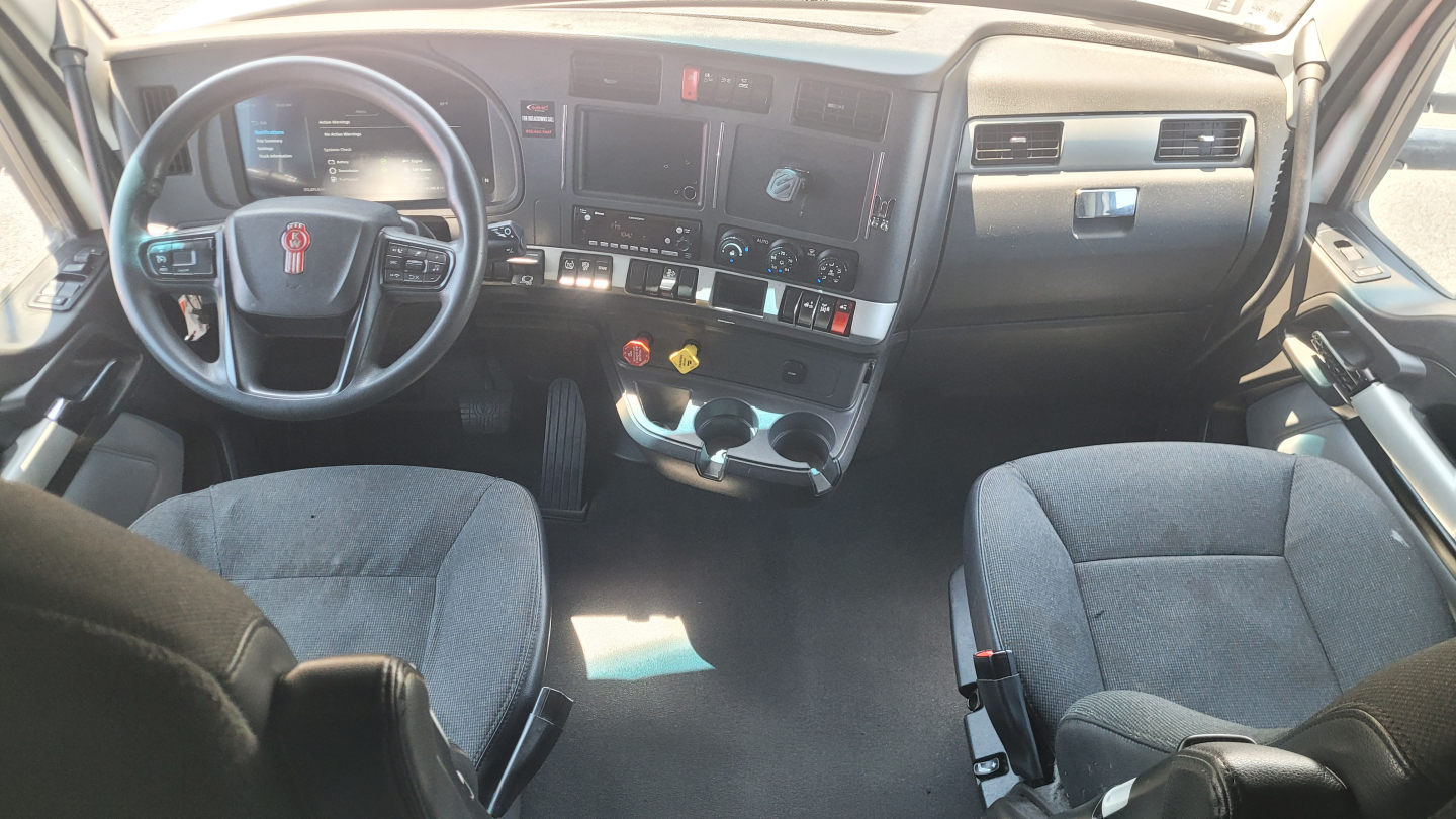 Kenworth T680 truck cabin dashboard and steering wheel with two seats, control switches, and digital displays visible.