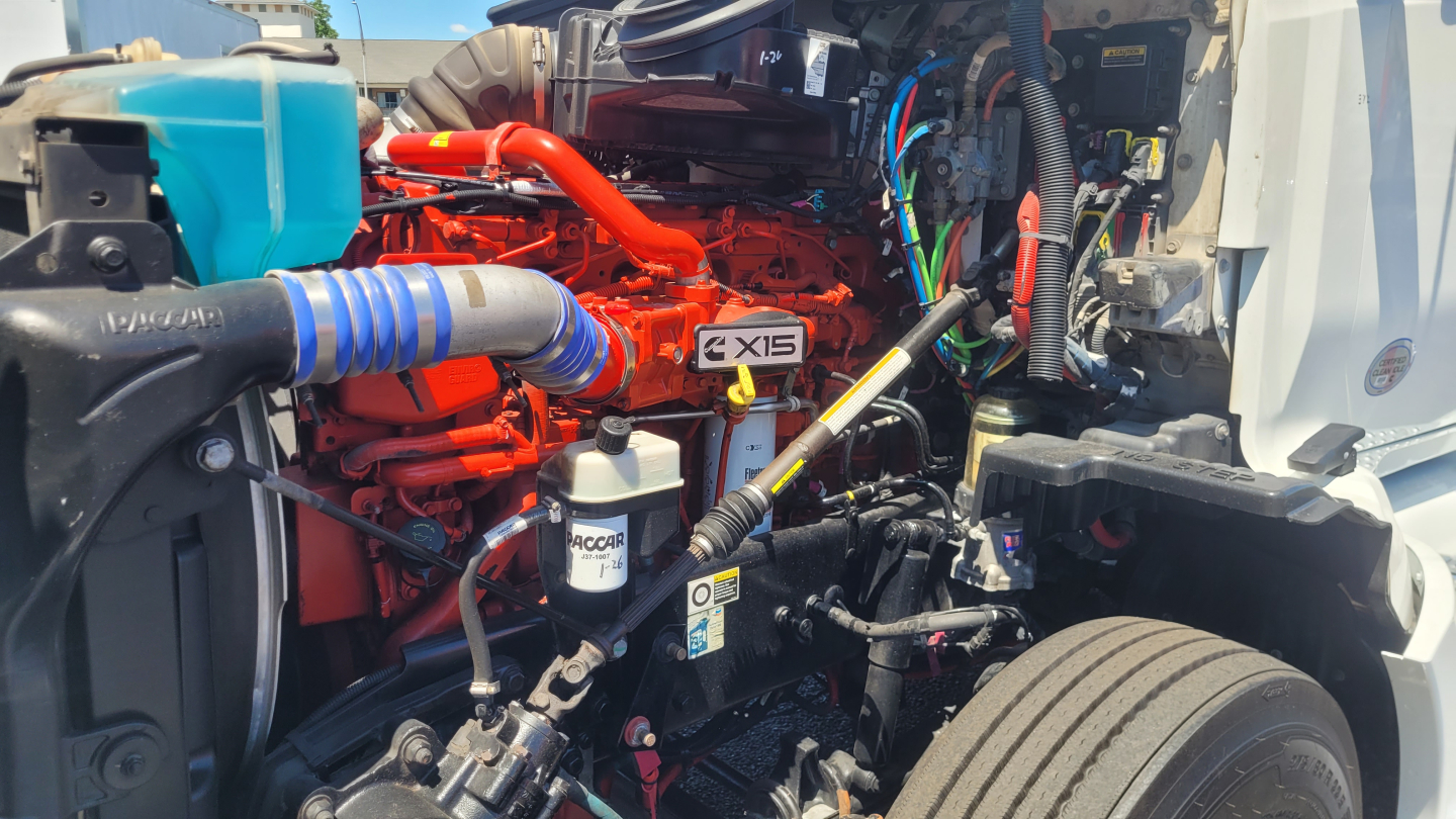 Kenworth T680 engine bay showing orange engine block and various hoses and wiring.