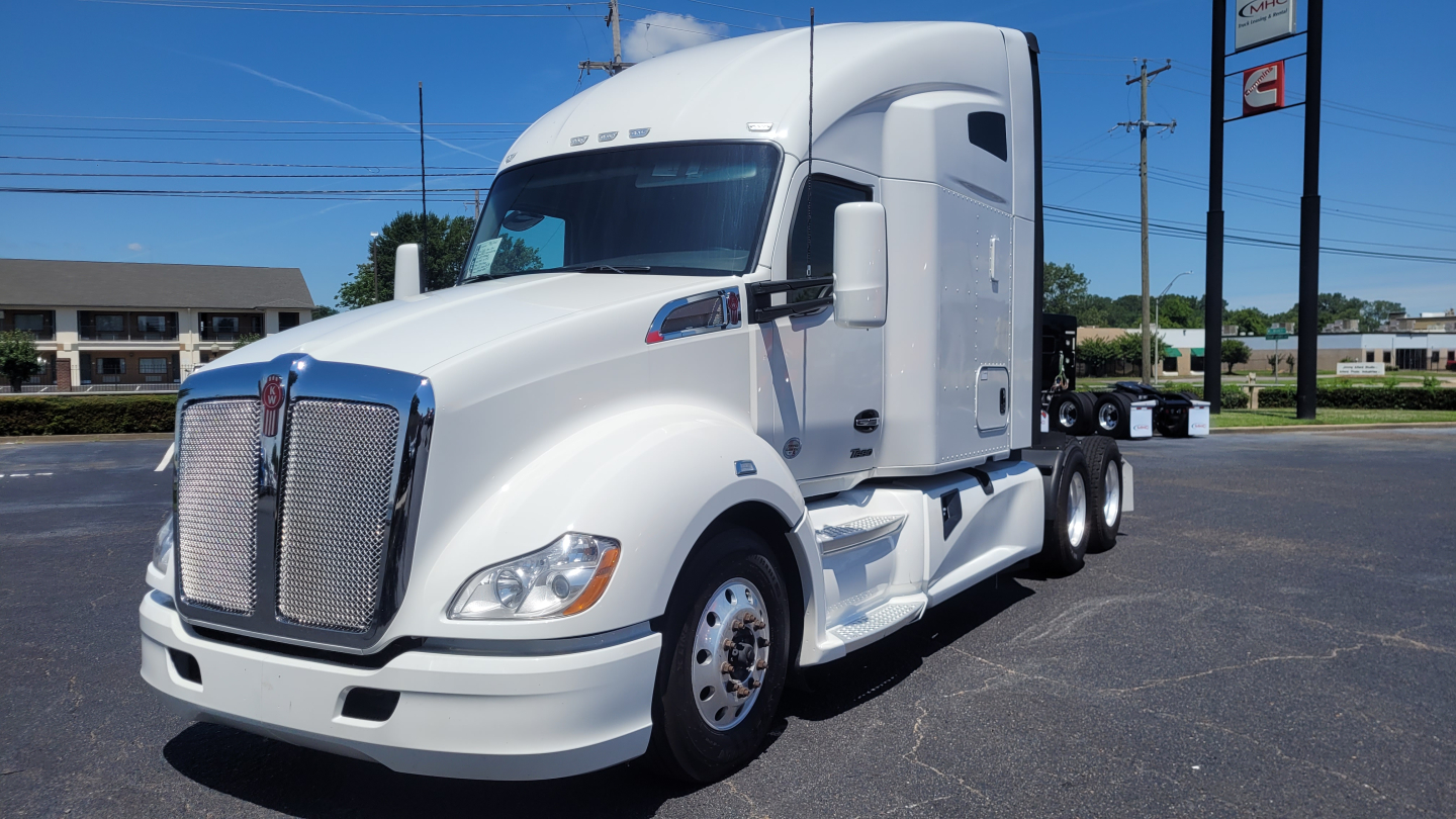 Kenworth T680 sleeper cab truck in white, front-left view, chrome grille, dual rear axles, daytime outdoor lot
