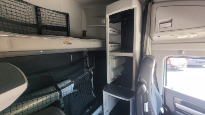 Kenworth T680 cab interior showing sleeper bunk area with overhead storage and open closet/storage compartments.