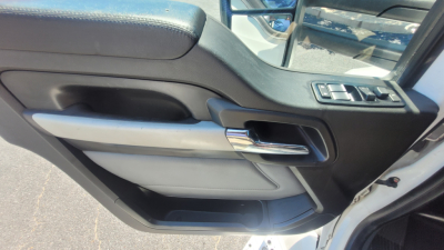 Truck door panel of a 2022 Kenworth T680 showing power window controls, chrome door handle, black interior, light gray armrest, and storage pocket.