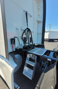 Kenworth T680 engine bay area showing access steps and cab area, with hoses and electrical connectors visible near the entry.