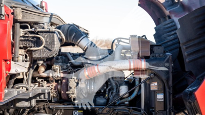 Kenworth T680 engine bay showing large turbocharger, intercooler piping, hoses, and engine components in a truck cab with red exterior.