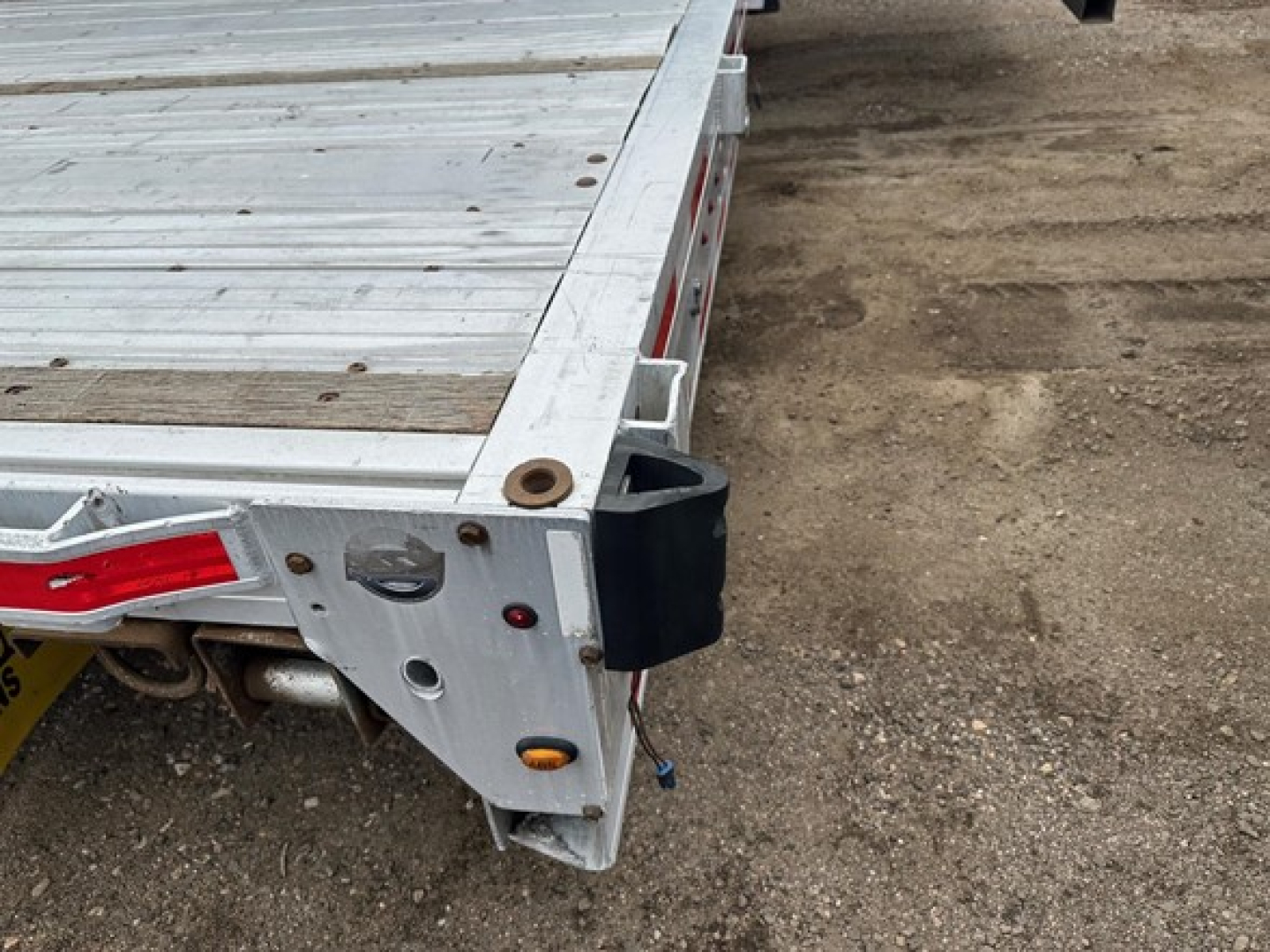 Drop deck trailer corner showing aluminum bed, rear corner with tail light and modular fitting. Visible are aluminum surface, side rail, and black bumper or bumper cover.