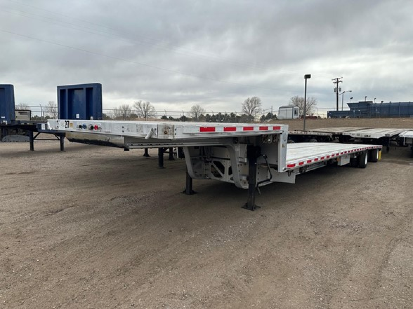 All-aluminum Trail King drop deck trailer with extendable gooseneck and multiple axles, side rails, and warning lights. Flatbed surface visible with landing gear down.