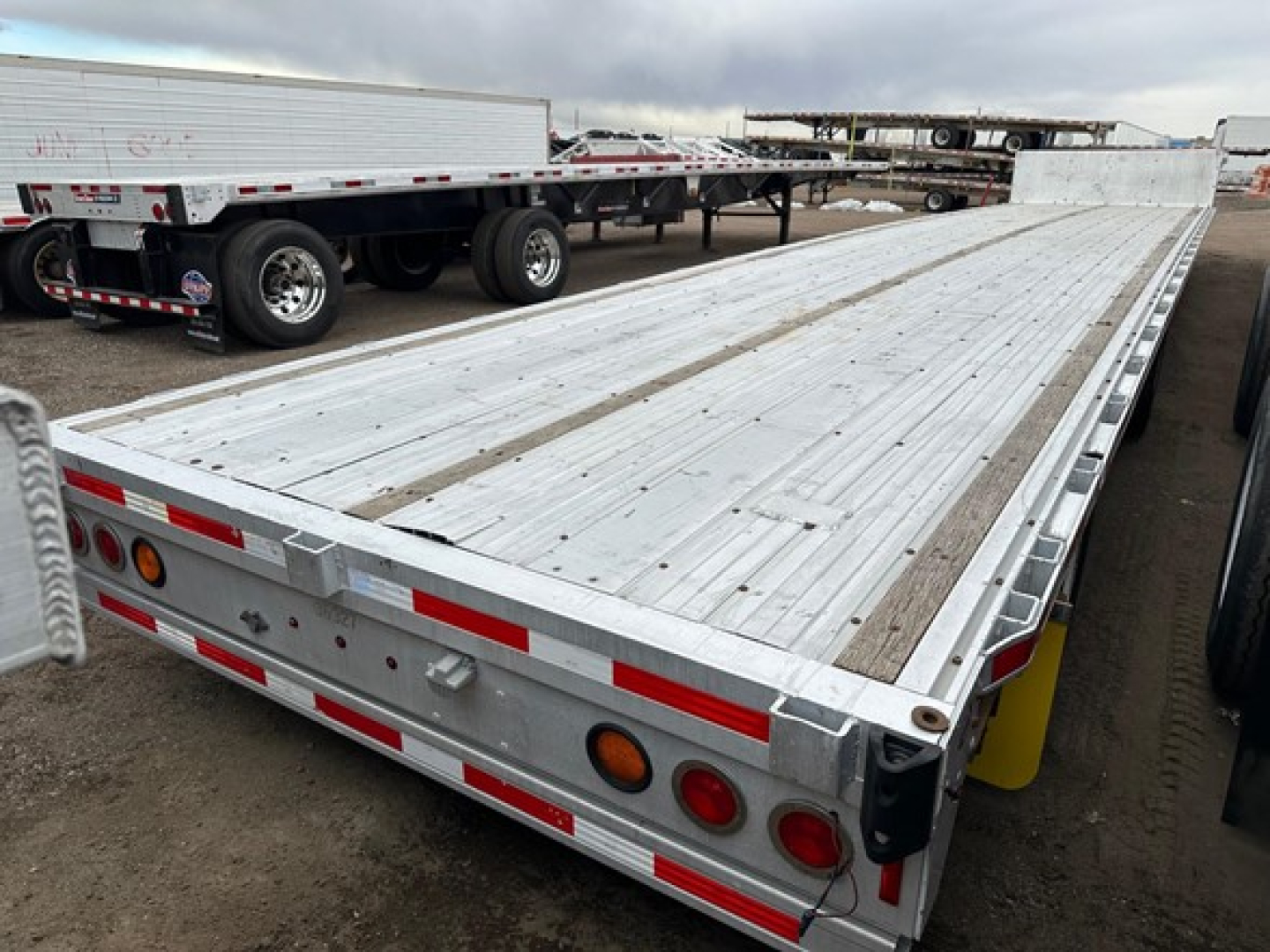 Trailer rear of an all-aluminum drop deck trailer showing long flat deck, aluminum plank surface, taillights, and reflective striping.