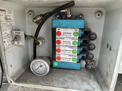 Trail King trailer control panel with blue switch box showing ON/OFF, UN-LOCKED/LOCKED, RAIS E, DUMP, TRANSPORT, and gaug e in cabinet interior.