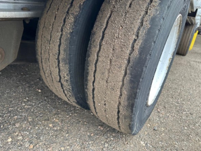 Trailer tire pair on a Trail King all aluminum drop deck trailer showing dual rear tires and gravel road surface.
