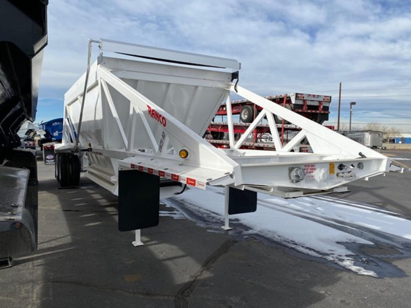 Dump trailer showing RANCO LW21-40 steel frame, white paint, triangular truss side rails, hopper tub with chute, and support legs. Visible text 'RANCO' on side.