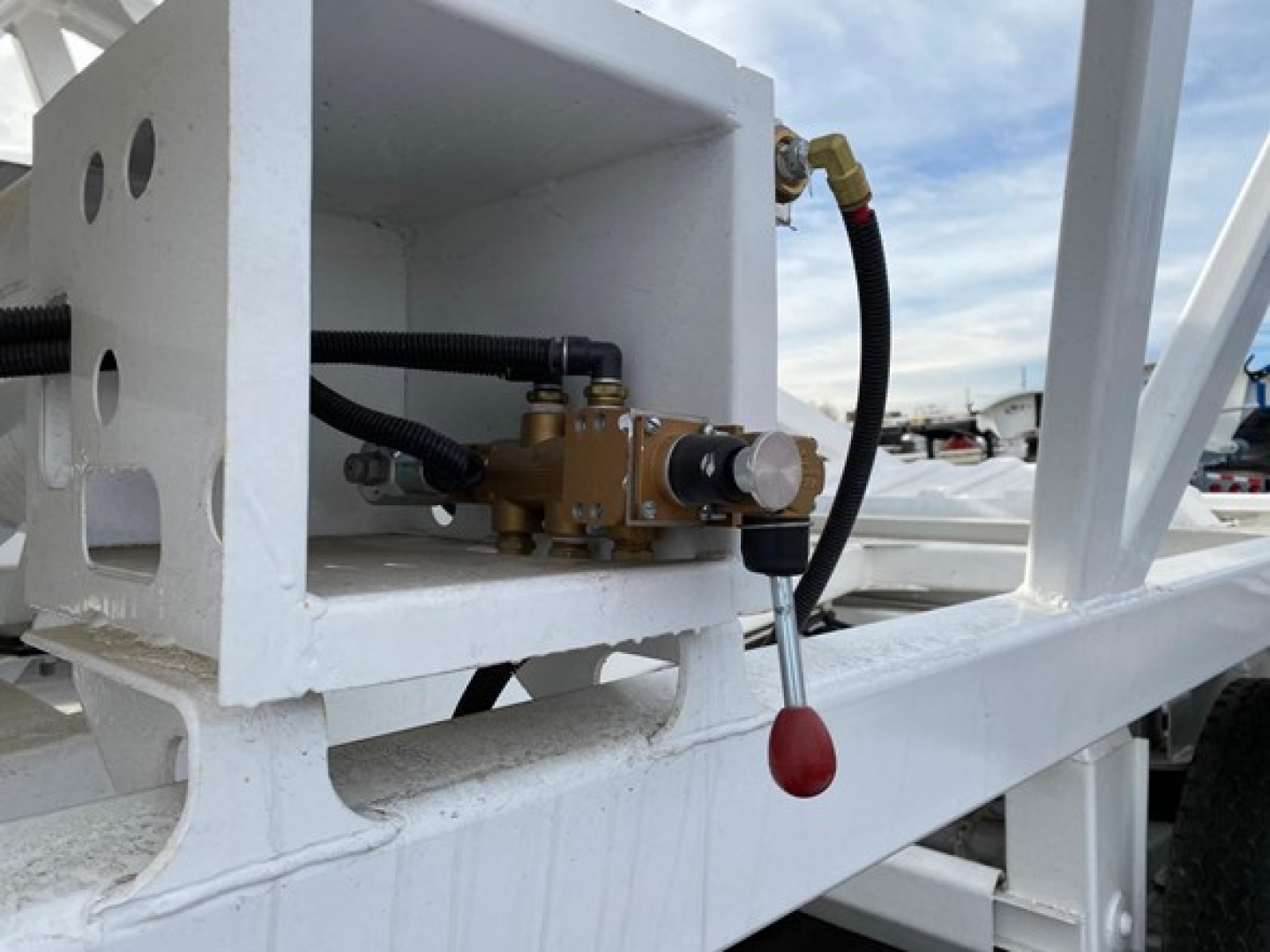 Dump trailer hose valve assembly mounted in a white frame with hydraulic lines and a red-handled valve knob.