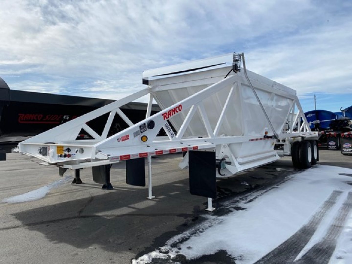 Dump trailer showing Ranco LW21-40 frame with triangle lattice and dual axles. Visible text includes RAND0 on side and various safety labels; white color.
