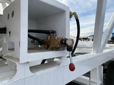 Valve assembly and hydraulic hose on a white dump trailer frame, with a red-handled lever and brass hydraulic component mounted inside a square cutout.