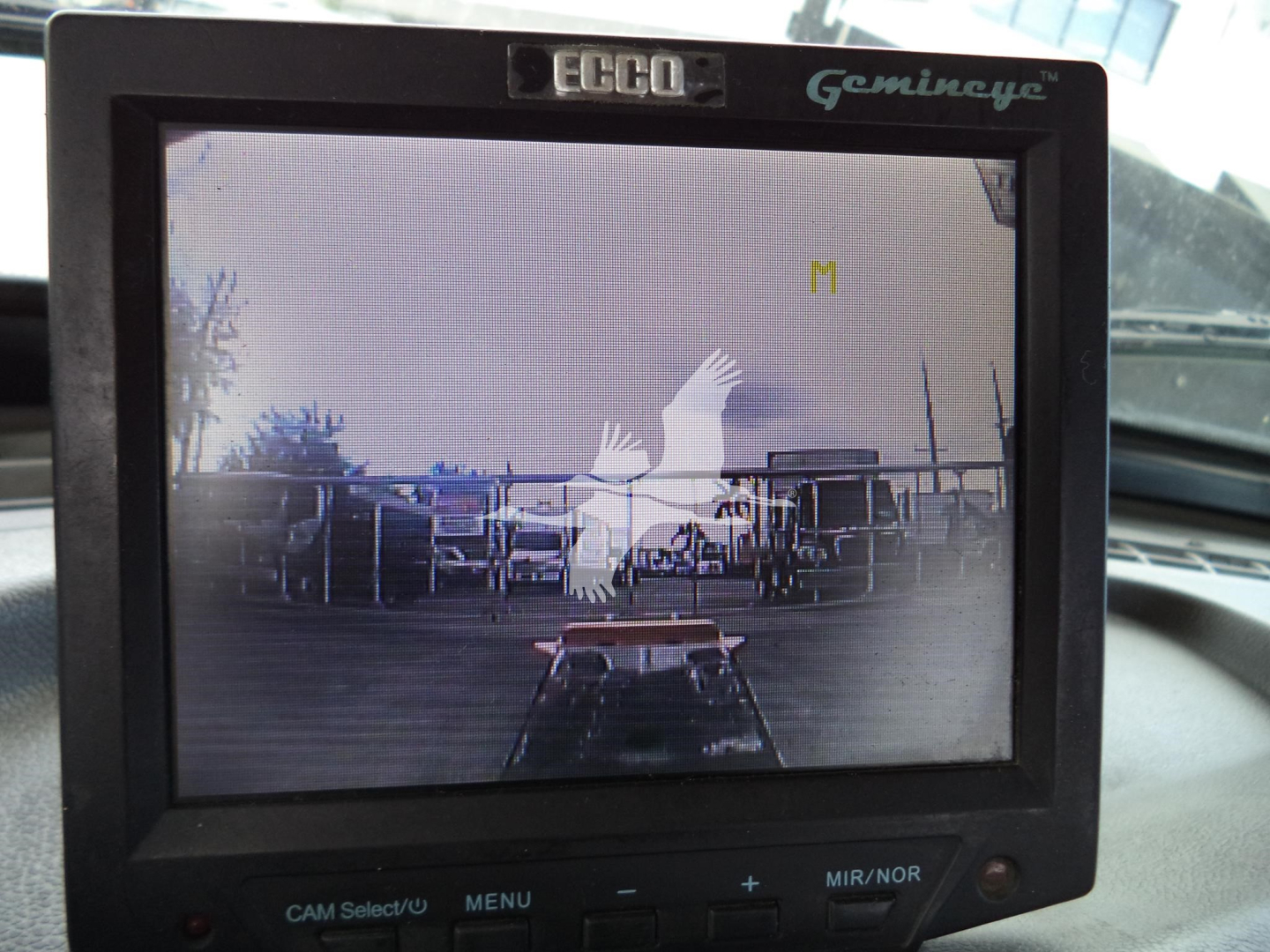 Vehicle rear view camera display in Peterbilt 348 cab showing yard with equipment silhouettes and a bird watermark, ECO Gemanice label on monitor.