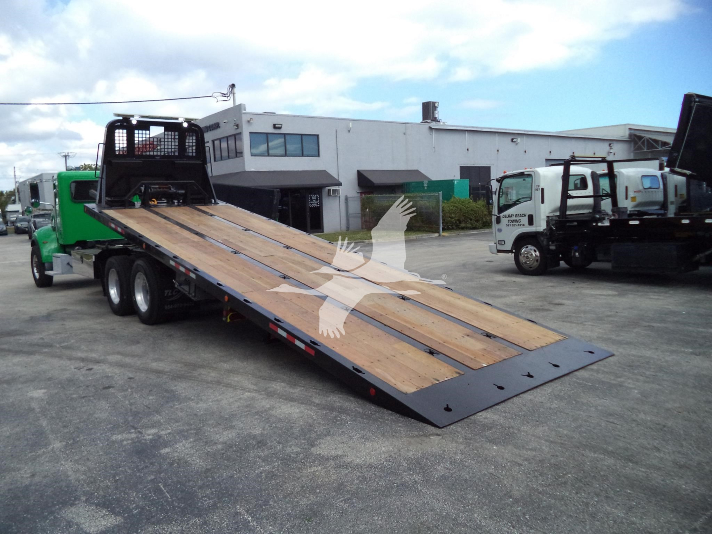 Peterbilt 348 rollback truck with a lowered wooden deck ramp in a dealership lot.