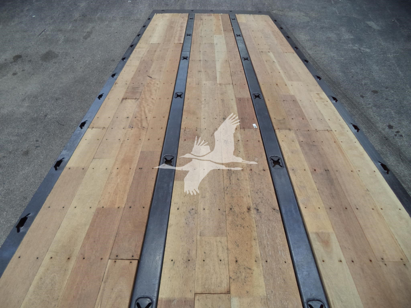 Truck bed showing wooden deck with metal frame rails and a white bird logo overlay.