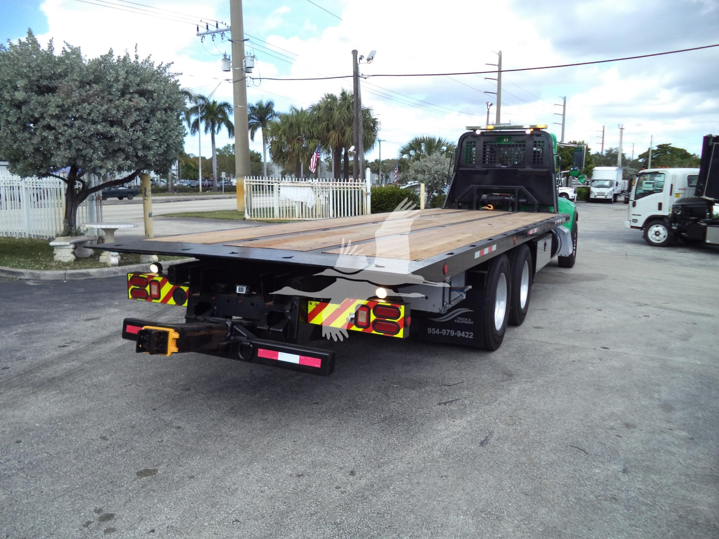 Rear view of a black flatbed rollback tow truck with wooden deck and yellow/red reflective chevrons.
