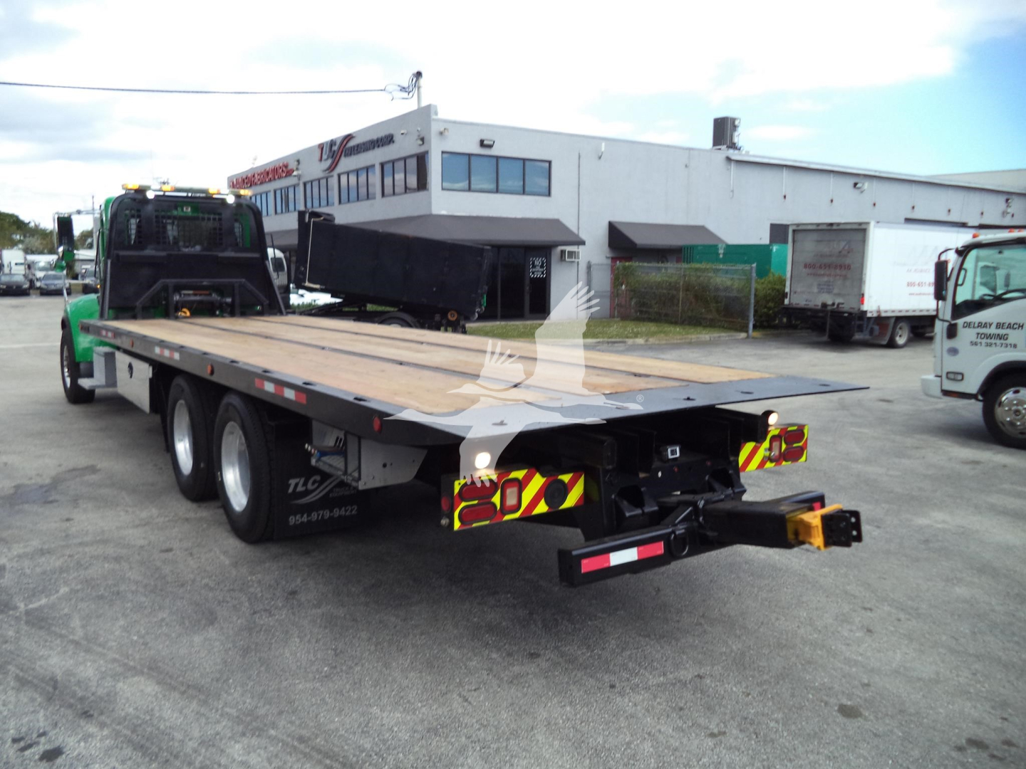 Peterbilt 348 rollback truck with flatbed trailer viewed from rear left, showing wooden deck, triple rear axles, and reflective rear lights.