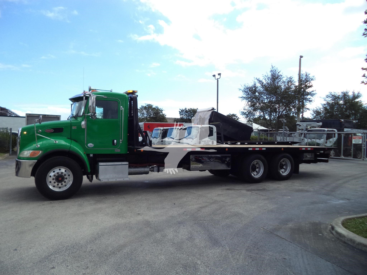 Peterbilt 348 rollback truck in green showing long flatbed with a folded ramp and hydraulic mech.