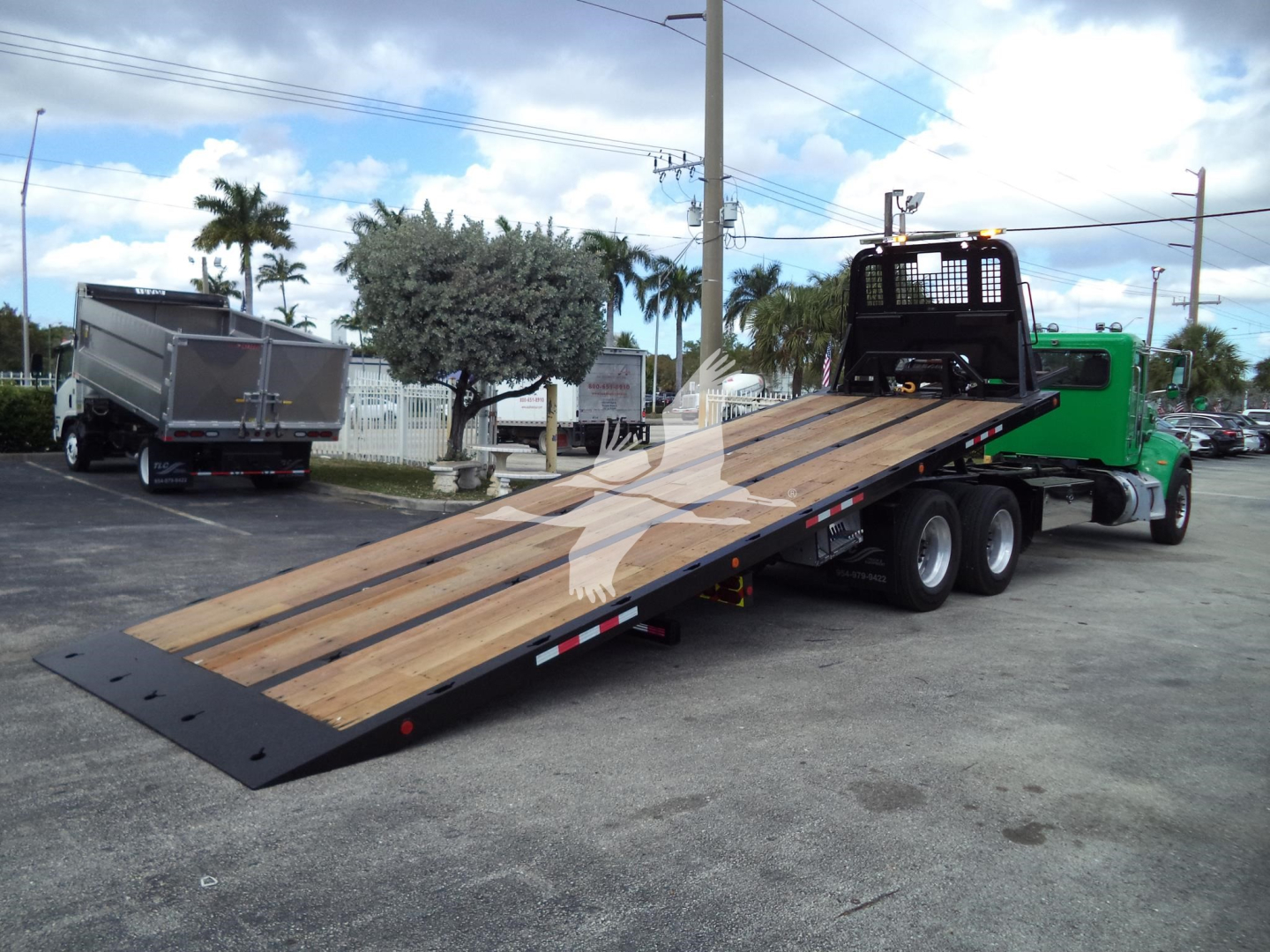 Peterbilt 348 rollback truck with wood deck extended in trailer position and green cab.