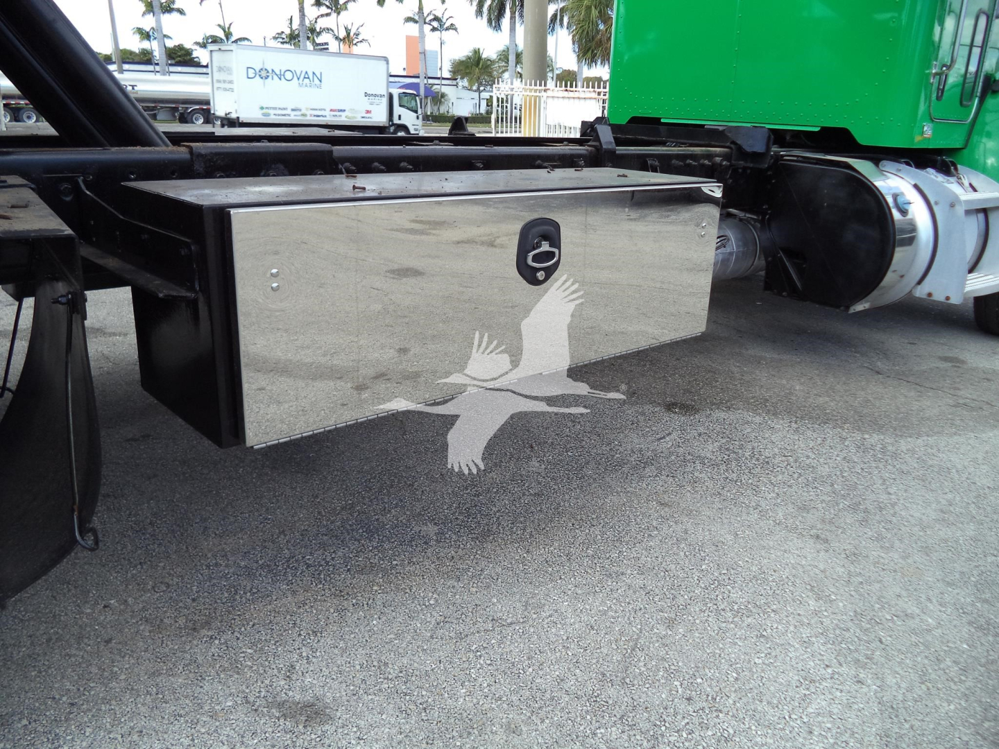 Trailer hitch/payload area with a shiny metal toolbox mounted under a Peterbilt chassis; view shows external tool storage box with rounded edges and a lock, on a rollback truck.