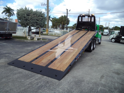 Truck bed of a 2016 Peterbilt 348 rollback trailer with wooden deck and black steel rails, rear of truck visible